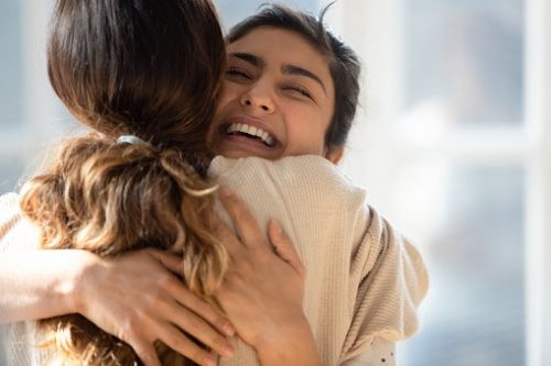 Two women are hugging each other to show support. The woman with the smiling face looks happy and relieved. 